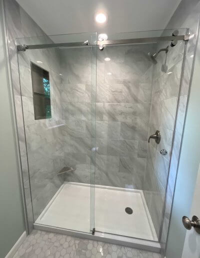 frameless glass shower door with white and grey ceramic tile walls