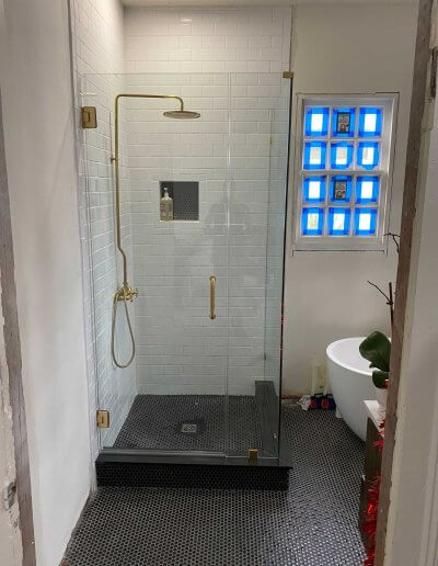 frameless glass shower enclosure with white walls and gold water fixture